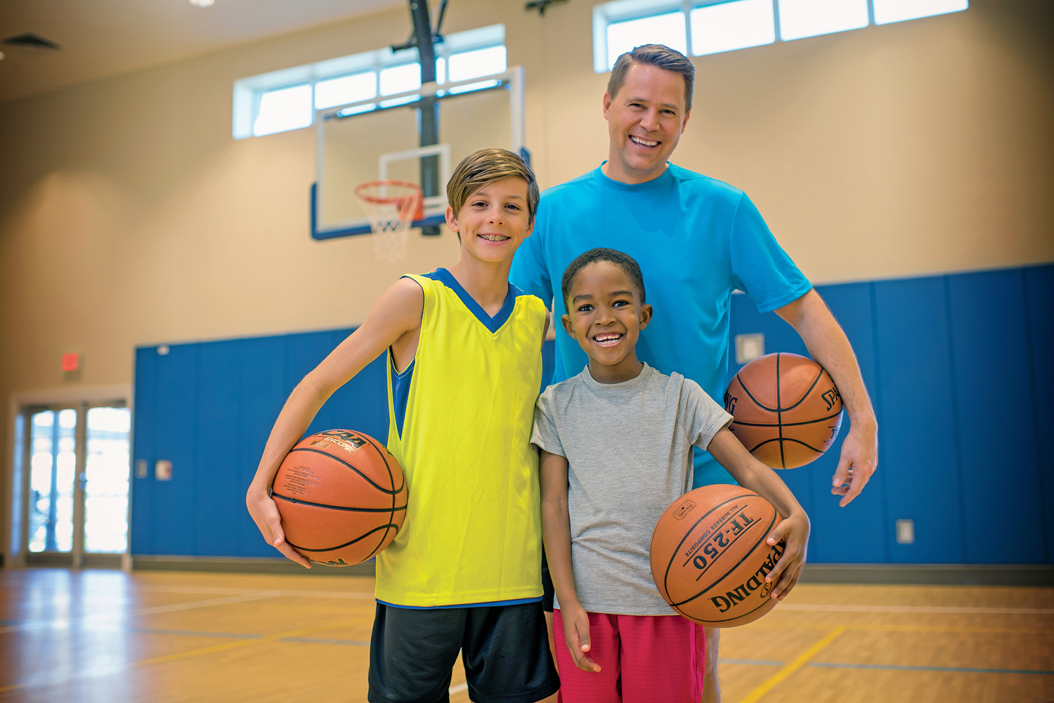 A man and two boys with basketballs smiling and posing for camera.