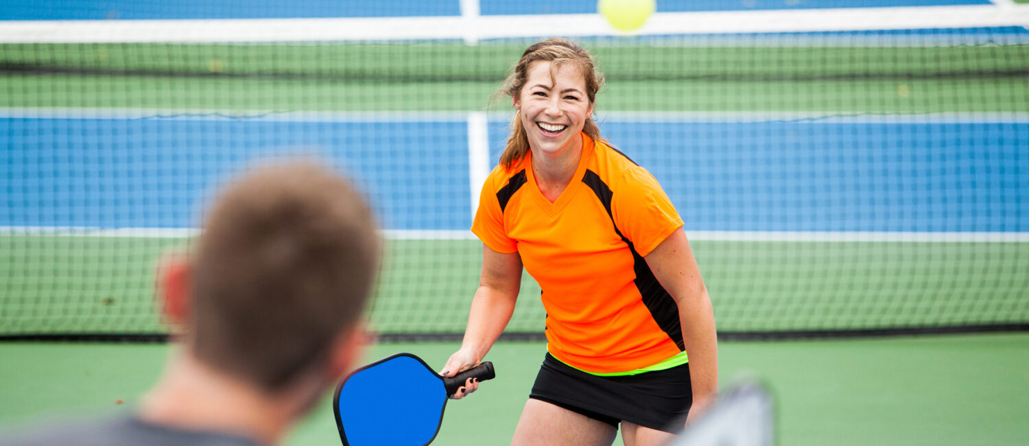 Female Pickleball player is returning a serve on an outdoor court.