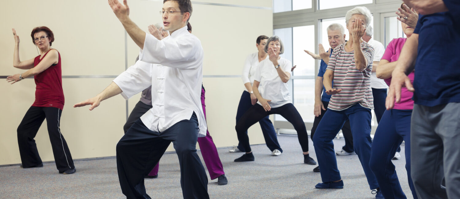 Group of senior adults practicing tai chi with an instructor in the community center., blurred motion.