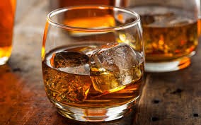 glass of bourbon with ice on a wooden counter